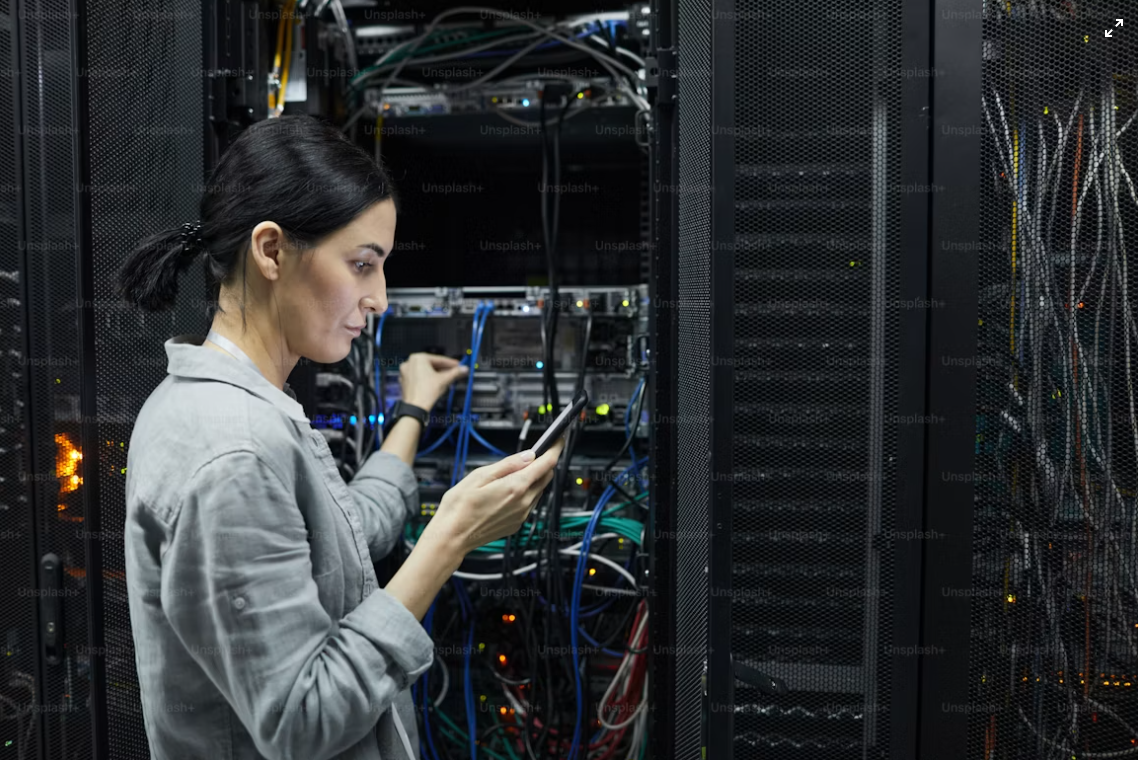 An engineer checking a tablet against a live rack of cabled switches in a data center aisle