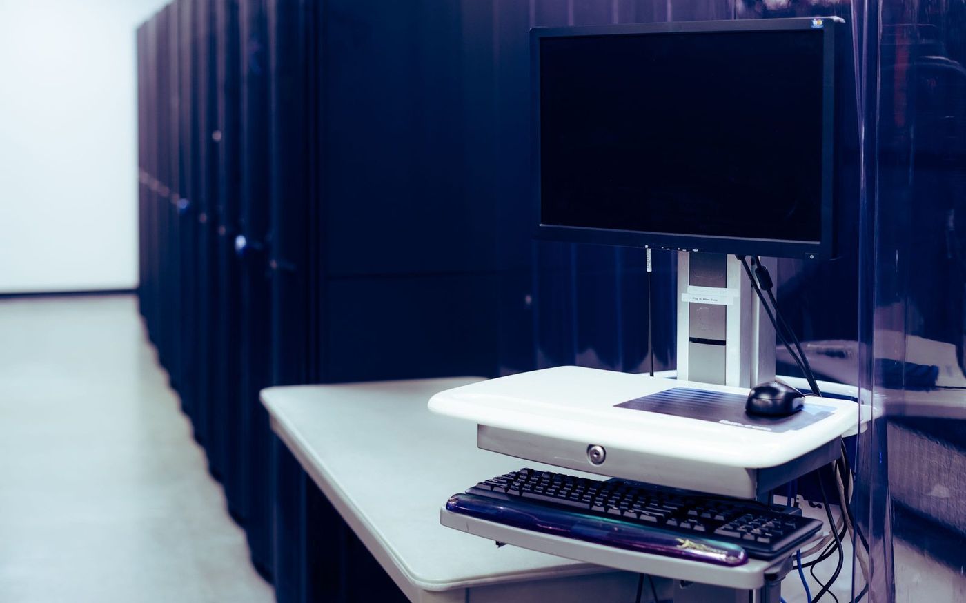 A crash cart with a monitor and keyboard parked beside a row of closed server cabinets